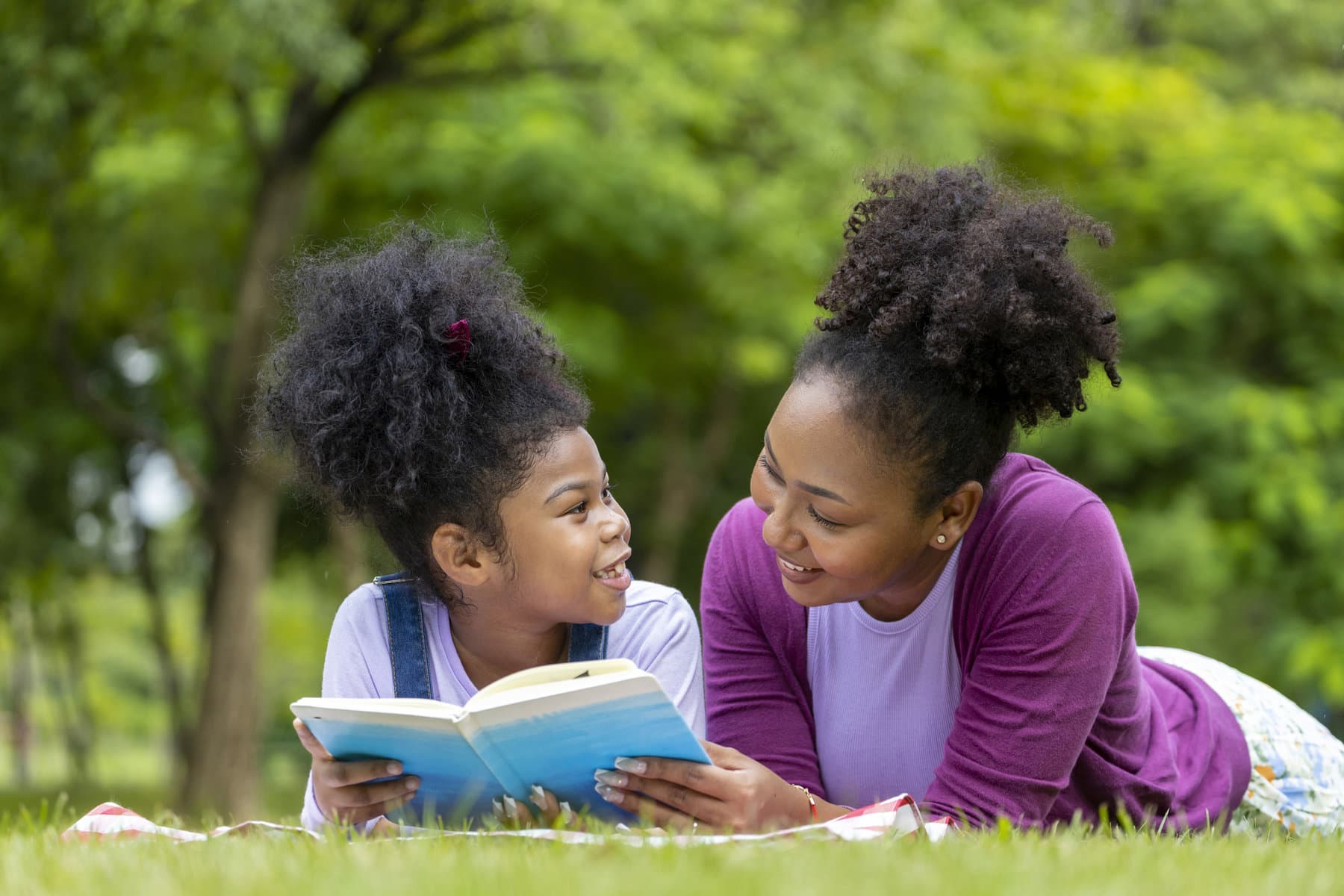 mother and daughter reading a book outside in summer