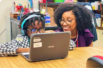 Teacher with student working on laptop and smiling