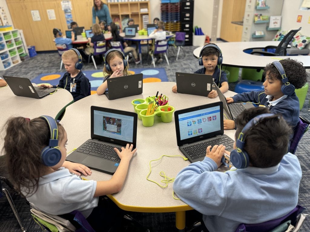 Students in a classroom wearing headphones and working on laptops.